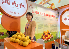 湖南湘九红农业科技有限公司主要的朱经理在展位前展示公司主打产品石门柑橘。/ Manager Zhu from Hunan Xiangjiuhong Agricultural Technology Co., Ltd. displays the company's flagship product, Shimen citrus, in front of the booth.