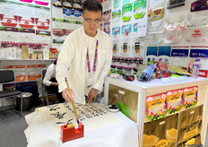 来自东菀市长荣佳胶袋有限公司的董事长在展位用毛笔写字。公司制造各种胶袋，铝箔袋/纸袋和生物降解袋。/ The chairman of Dongwan Gao Zhiyuan Plastic Productions Ltd. in Dongwan City is writing calligraphy at the booth. The company manufactures a variety of plastic bags, aluminum foil bags, paper bags, and biodegradable bags.