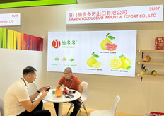 厦门柚多多进出口有限公司的参展代表（右一）正在和到访客商进行会谈。/ The exhibition representative from Xiamen Youduoduo Import and Export Co., Ltd. (first from the right) is talking with the visitor.