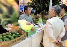 八方牛油果公司的负责人王先生（左一）正在与到访客商进行交谈。/ Mr. Wang (first from left), the head of Bafang Avocado Company, is talking with visitors.